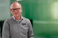 Ett porträtt av en leende man med glasögon, klädd i en grå tröja över en skjorta med en namnskylt där det står "avonova". Han sitter i en ljus kontorsmiljö med en suddig, grön vägg i bakgrunden som ger en professionell och förtroendeingivande känsla.