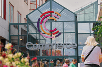 Entrén till köpcentrumet Commerce med en färgstark C-logotyp på glastaket och besökare i förgrunden.
