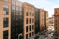 Moderna kontorsbyggnader i tegel och glas som kantar en stenlagd gata i ett urbant område under en klar himmel.