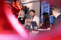 Paneldeltagare diskuterar på scen framför en presentationsskärm och röda sifferballonger.
