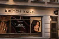 Butiksfasad i ögonhöjd för "SWITCH NAILS" med belyst skyltning, stora kampanjfönster och en entrédörr under dämpad kvällsbelysning.