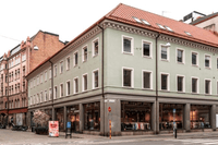 Exteriör av en ljust grön hörnbyggnad i tre våningar med butikslokaler i markplan och ett rött tegeltak, belägen vid en gata.