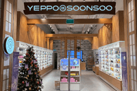 Entrén till en butik för koreansk skönhetsvård med ljusa trädetaljer, välfyllda hyllor med hudvårdsprodukter och en pyntad julgran i förgrunden.