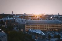 En flygbild över Sickla i Stockholm under solnedgången, med Sickla köpkvarter i förgrunden och stadens silhuett, inklusive Globen, i fjärran.