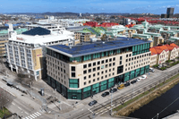 Flygfoto över ett torg- och stadsområde med en modern vinkelbyggnad i förgrunden, Scandic-hotell intill samt en kanal till höger.