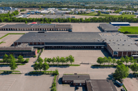 Flygfoto över ett stort industri- och logistikområde med mörkgrå lagerbyggnader, lastkajer och asfalterade ytor.