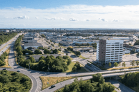 Högt flygfoto över ett industri- och handelsområde med en modern, ljus kontorsfastighet, trafikerade vägar och grönområden under en klarblå sky