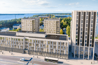 3D-visualisering i fågelperspektiv av moderna bostads- och kontorshus vid en väg nära en stor sjö eller havsbukt.