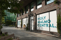 En vy av fasaden på Malmö Central i brunt tegel, skyltfönstret är täckt av en vit skyld när det står "Holy Malmö Central".