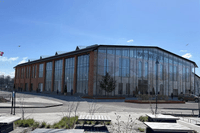 En stor industribyggnad i tegel med en modern glasfasad kallad Martinverket, omgiven av öppna ytor och bänkar under en klarblå himmel.