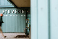 Entré till "STUVERIET" på Masthamnsgatan 21 med ljusgrön räfflad fasad och en förbigående person i rörelse oskarp i förgrunden