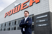 En man i mörk kavaj står med korsade armar framför Power-butikens fasad och skyltning.