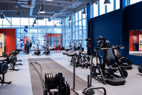 Ett modernt och rymligt gym från Fitness 24 Seven med styrketräningsmaskiner, roddmaskiner, battleropes och stora fönster.