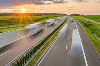 Lastbilar i rörelse på en motorväg genom ett öppet landskap under en färgstark solnedgång.