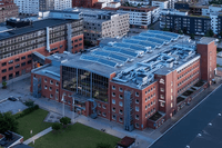 Den stora tegelbyggnaden har ett modernt glaskonstruerat mittparti och taket är täckt med solcellspaneler. Byggnaden ligger i ett urbant område nära hamnen med flertalet bostadshus i bakgrunden.