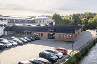 Flygfoto i fågelperspektiv över en tegelbyggnad med skylten BRANDTOWN, intilliggande parkeringsplats med bilar och ett vattendrag.