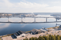 Flygfoto över ett vattendrag med en lång bro och ett industri- samt handelsområde i förgrunden.