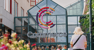 Entrén till köpcentrumet Commerce med en färgstark C-logotyp på glastaket och besökare i förgrunden.