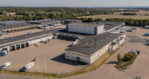 Flygfoto i fågelperspektiv över ett stort logistik- och lagerkomplex med lastkajer, lastbilar och omgärdande åkermark.