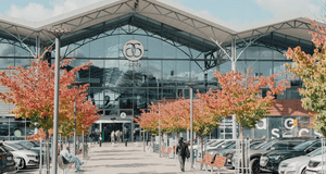 Exteriör av köpcentret Asecs i Jönköping under en solig höstdag, med färgstarka träd framför huvudentrén och parkerade bilar i förgrunden.