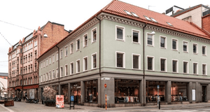 Exteriör av en ljust grön hörnbyggnad i tre våningar med butikslokaler i markplan och ett rött tegeltak, belägen vid en gata.