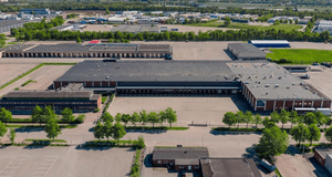 Flygfoto över ett stort industri- och logistikområde med mörkgrå lagerbyggnader, lastkajer och asfalterade ytor.