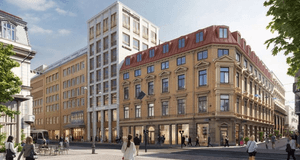 En stadsgata med människor som promenerar och sitter vid uteserveringar, omgiven av större byggnader i olika stilar. I förgrunden syns ett hörnhus i klassisk arkitektur med ljus fasad och rött tak, medan en modernare byggnad i glas och tegel reser sig bak