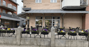 Fasaden till ett bageri, konditori och café med en uteservering i förgrunden, prydd med blomlådor fyllda med färgglada penséer.