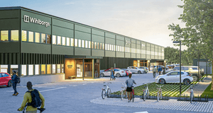 En digital visualisering av en lång, grön industrifastighet med Wihlborgs logotyp på fasaden. Framför byggnaden syns en parkeringsplats med bilar, cykelställ och människor i rörelse.
