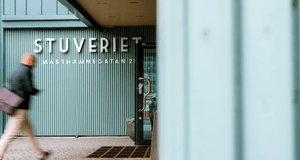 Entré till "STUVERIET" på Masthamnsgatan 21 med ljusgrön räfflad fasad och en förbigående person i rörelse oskarp i förgrunden
