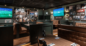 Interiör av en sportbar med dämpad belysning, mörkgröna väggar och bruna lädersoffor i bås. Väggarna är tätt dekorerade med inramade sportbilder, bland annat basket och ishockey, samt amerikanska vägskyltar för "Interstate 93" och "Beantown". Flera stora 