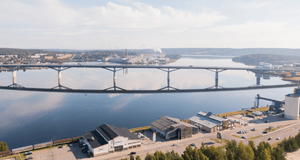 Flygfoto över ett vattendrag med en lång bro och ett industri- samt handelsområde i förgrunden.