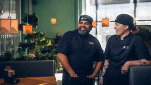 Två glada kockar i svarta arbetskläder och mössor från Sushi Yama står och samtalar i en restaurangmiljö.