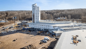 Vy över Navet i Jönköping under pågående markarbete och ombyggnation. Den vita byggnaden med sitt ikoniska torn syns bredvid en stor byggarbetsplats, med skogsklädda höjder i bakgrunden.