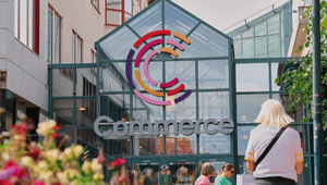 Entrén till köpcentrumet Commerce med en färgstark C-logotyp på glastaket och besökare i förgrunden.