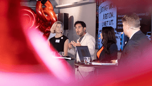 Paneldeltagare diskuterar på scen framför en presentationsskärm och röda sifferballonger.