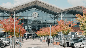 Exteriör av köpcentret Asecs i Jönköping under en solig höstdag, med färgstarka träd framför huvudentrén och parkerade bilar i förgrunden.