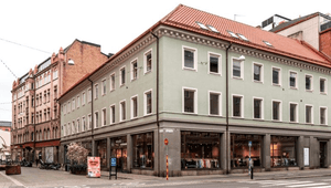 Exteriör av en ljust grön hörnbyggnad i tre våningar med butikslokaler i markplan och ett rött tegeltak, belägen vid en gata.