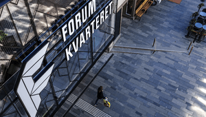 Flygbild ovanför entrén till Forumkvarteret med en gående person på det stensatta torget nedanför.
