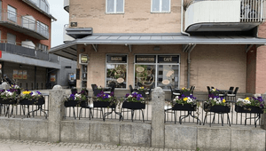Fasaden till ett bageri, konditori och café med en uteservering i förgrunden, prydd med blomlådor fyllda med färgglada penséer.