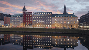En rad vackra fastigheter längs kanalen i Malmö, inklusive den röda tegelbyggnaden "Hjörne" och Volito Fastigheters huvudkontor. Byggnaderna och den rosa kvällshimlen speglar sig i det stilla vattnet vid skymning.