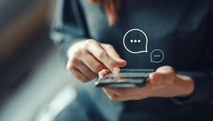 Närbild på en persons händer som använder en smartphone, med grafiska pratbubblor som svävar ovanför skärmen för att illustrera textmeddelanden eller chatt.