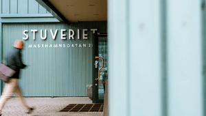 Entré till "STUVERIET" på Masthamnsgatan 21 med ljusgrön räfflad fasad och en förbigående person i rörelse oskarp i förgrunden