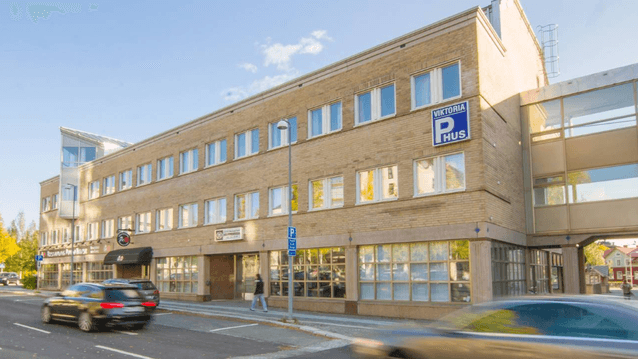 Exteriör av Viktoria P-hus, en flervåningsbyggnad i gult tegel med en inglasad gångbro, belägen vid en gata med passerande bilar.