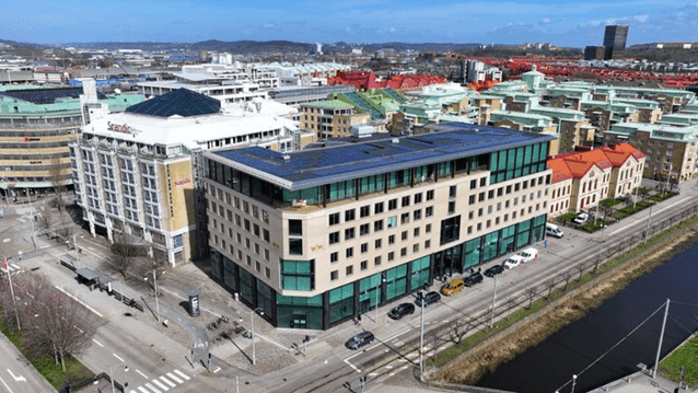 Flygfoto över ett torg- och stadsområde med en modern vinkelbyggnad i förgrunden, Scandic-hotell intill samt en kanal till höger.