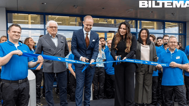 En gruppbild tagen utomhus framför entrén till en Biltema-butik, med logotypen synlig i det övre högra hörnet. Bilden visar en bandklippningsceremoni för invigningen av butiken (Biltema Bernstorp). Två män i kostym och en kvinna i mörka kläder står i mitt