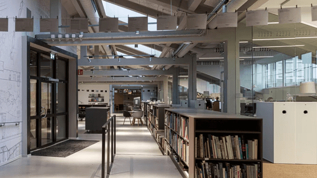 Ljust och modernt kontorsbibliotek med bokhyllor, öppna takbalkar och studieplatser i industriell design.