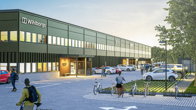 En digital visualisering av en lång, grön industrifastighet med Wihlborgs logotyp på fasaden. Framför byggnaden syns en parkeringsplats med bilar, cykelställ och människor i rörelse.