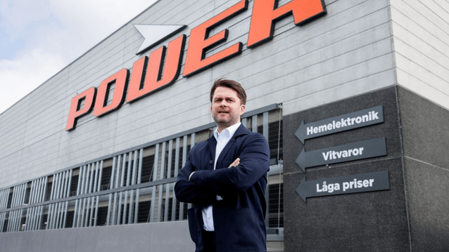 En man i mörk kavaj står med korsade armar framför Power-butikens fasad och skyltning.