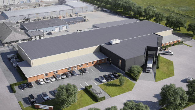 En digital visualisering av en stor industrifastighet sedd från ovan. Byggnaden har ett mörkt tak och ljusa fasader med en parkeringsplats full av bilar i förgrunden. En lastbil står parkerad vid en lastbrygga och området omges av gröna träd och gräsytor.